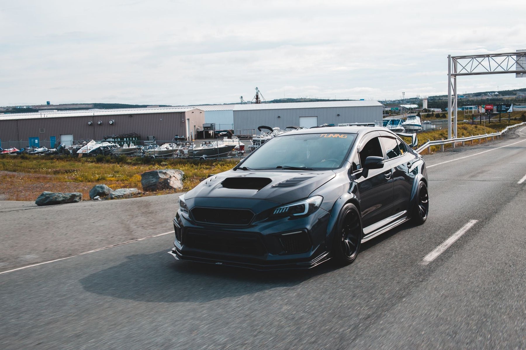 Expensive black tuned sports car with glossy surface and big front body kit riding on paved road out of city in daylight